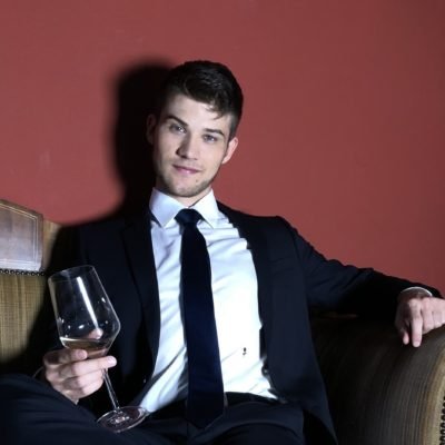 Hübsches Männermodell in schwarzem Anzug mit einem Glas Wein in der Hand